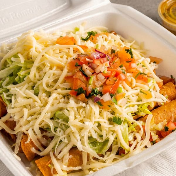Crispy taquitos in a takeout container, topped with shredded cheese, lettuce, pico de gallo, and a side of sauce.