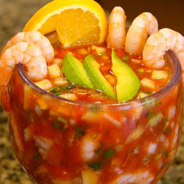 Vibrant shrimp cocktail in a glass, garnished with shrimp, avocado, and orange.