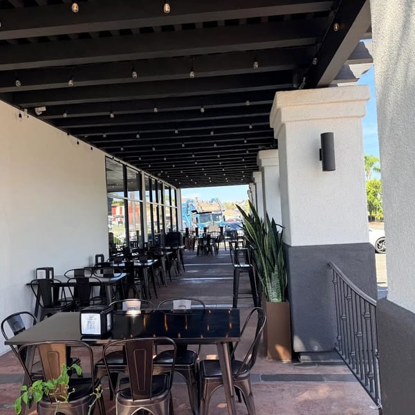 Outdoor patio dining area with black tables and chairs under a covered walkway with string lights.